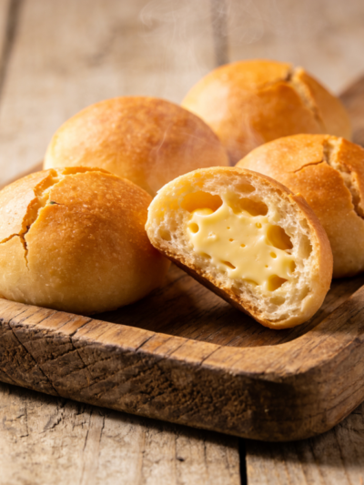 pão de queijo gostoso dourado com casca crocante e miolo puxento partido ao meio em bandeja de madeira