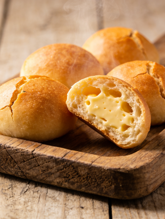 pão de queijo gostoso dourado com casca crocante e miolo puxento partido ao meio em bandeja de madeira