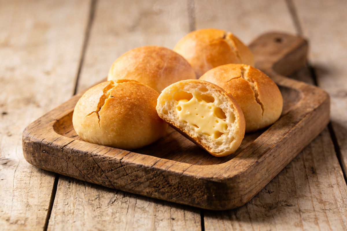 pão de queijo gostoso dourado com casca crocante e miolo puxento partido ao meio em bandeja de madeira