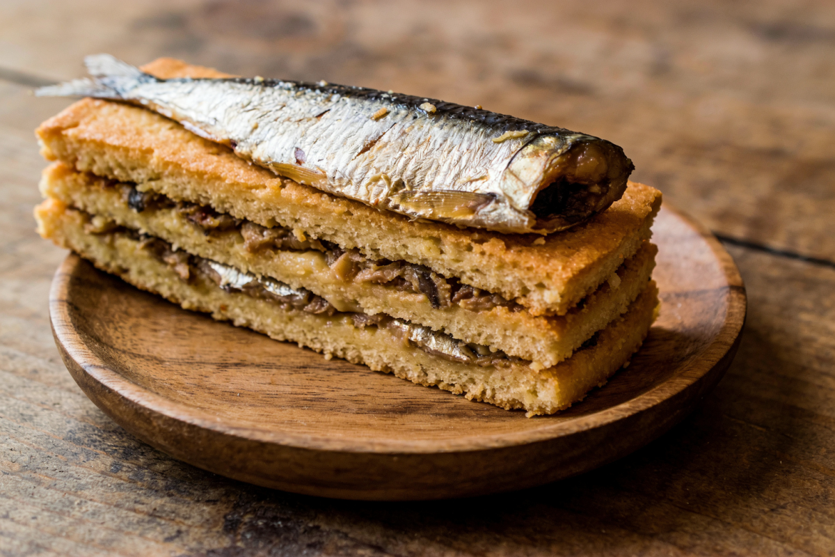 Fatia de bolo de sardinha fofinho com recheio de seleta e cheiro verde em prato de cerâmica
