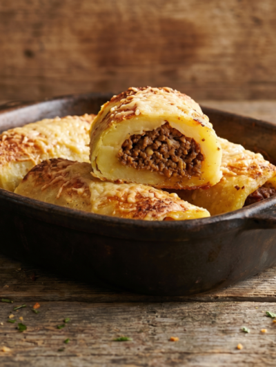 enrolado de carne moída dourado com queijo gratinado em assadeira, corte mostrando recheio suculento